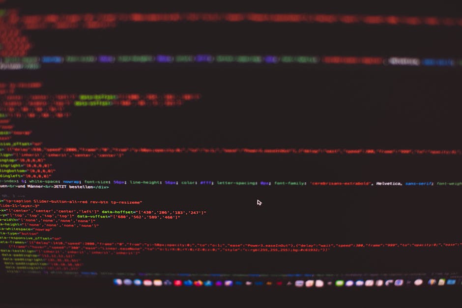 A close-up view of a person's hands typing on a laptop with a black keyboard, placed on a dark, smooth surface. The laptop screen displays a dark-themed coding interface with lines of multicolored cod